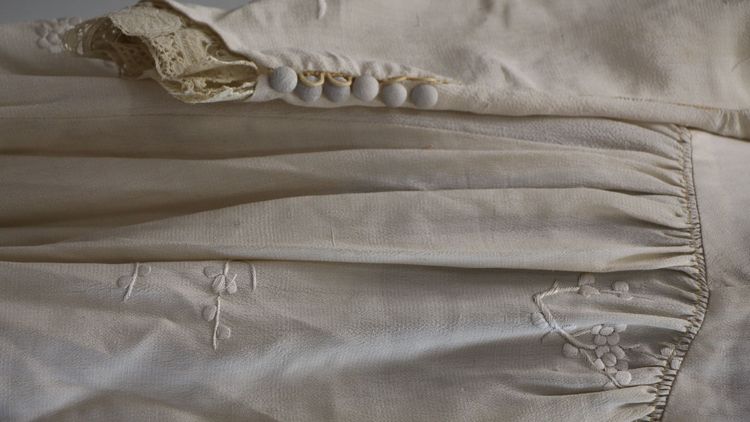 Das Foto zeigt ein altes Hochzeitskleid. Es ist weiß, hat aber Stockflecken vom Schweiß sowie andere Spuren der Nutzung.