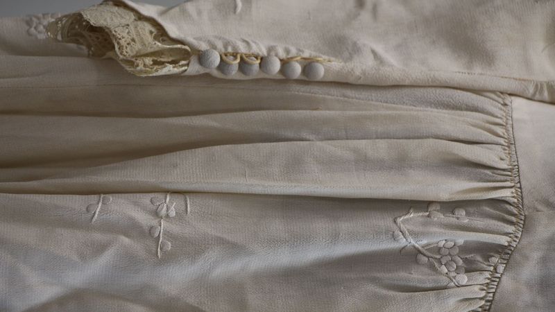 Das Foto zeigt ein altes Hochzeitskleid. Es ist weiß, hat aber Stockflecken vom Schweiß sowie andere Spuren der Nutzung.