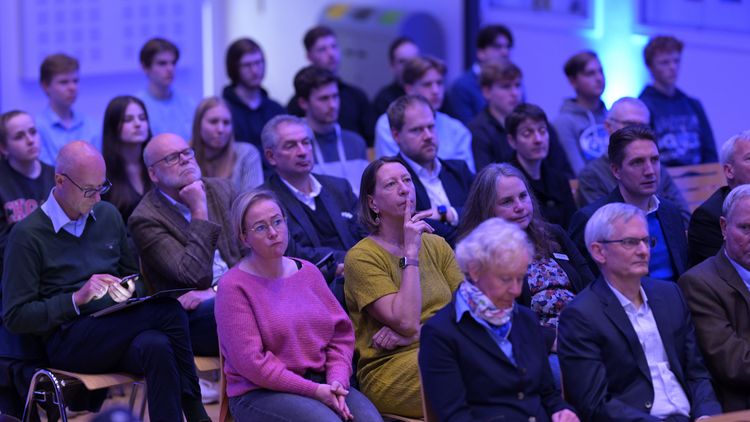 Das Bild zeigt das Publikum bei der Preisverleihung. Die Gäste sitzen auf Stühlen und schauen in Richtung Bühne. Der Saal ist in blaues Licht getaucht.