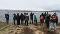 The photo shows several participants of the excursion. They are standing on the shore of a lake and looking into the distance. Several mountains can be seen on the misty horizon.