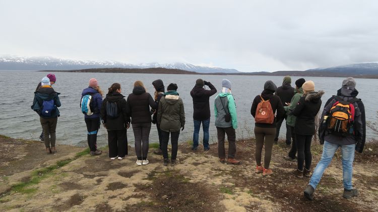 Das Foto zeigt mehrere Teilnehmende der Exkursion. Sie stehen am Ufer eines Sees und blicken in die Ferne. Am nebligen Horizont sind mehrere Berge zu erkennen.